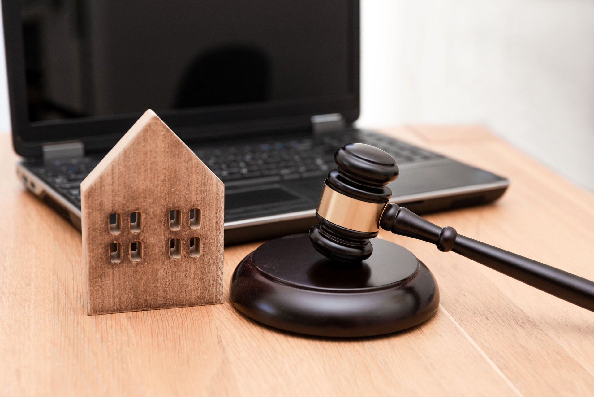 Wooden House Model and Judge Gavel on Desk with Laptop in the Background ,Real Estate Law or property law concept